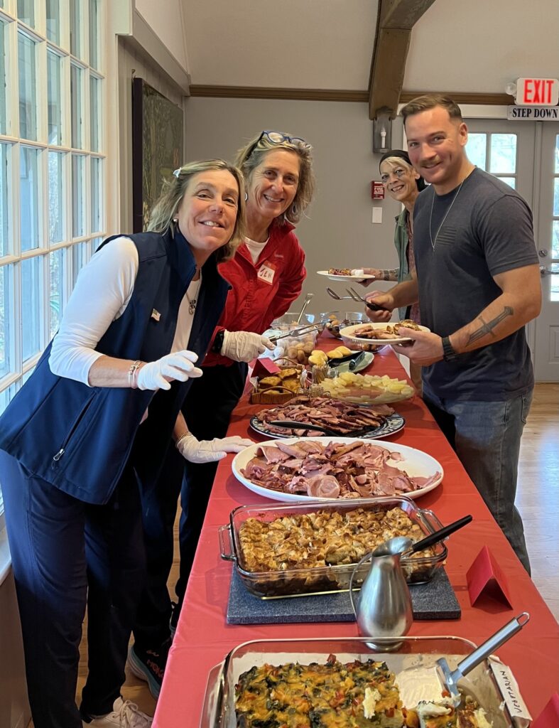 two women and and a young Veteran gathered over a table of potluck dishes